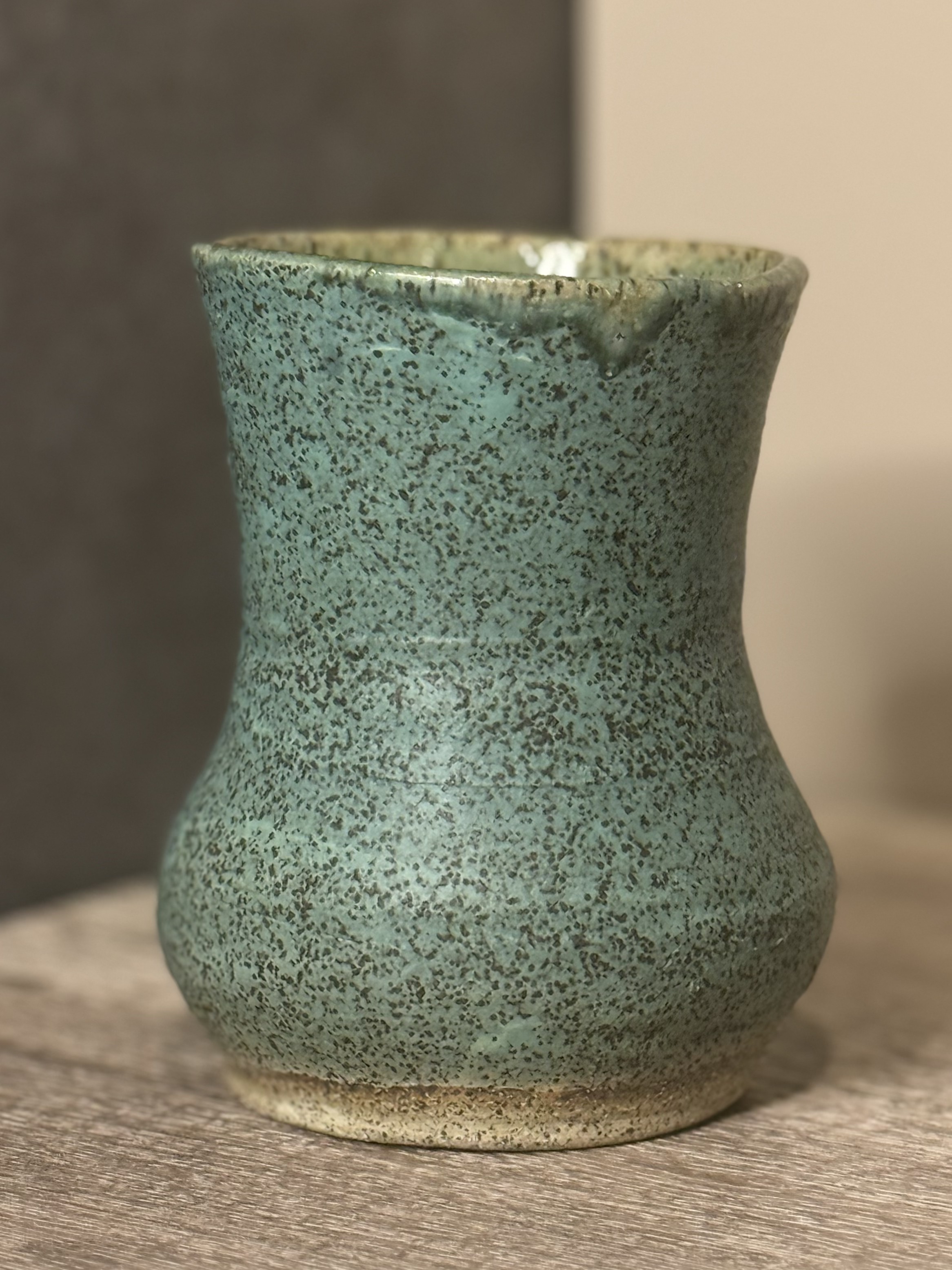 Speckled seafoam green ceramic vase with a soft hourglass shape on a wooden table
