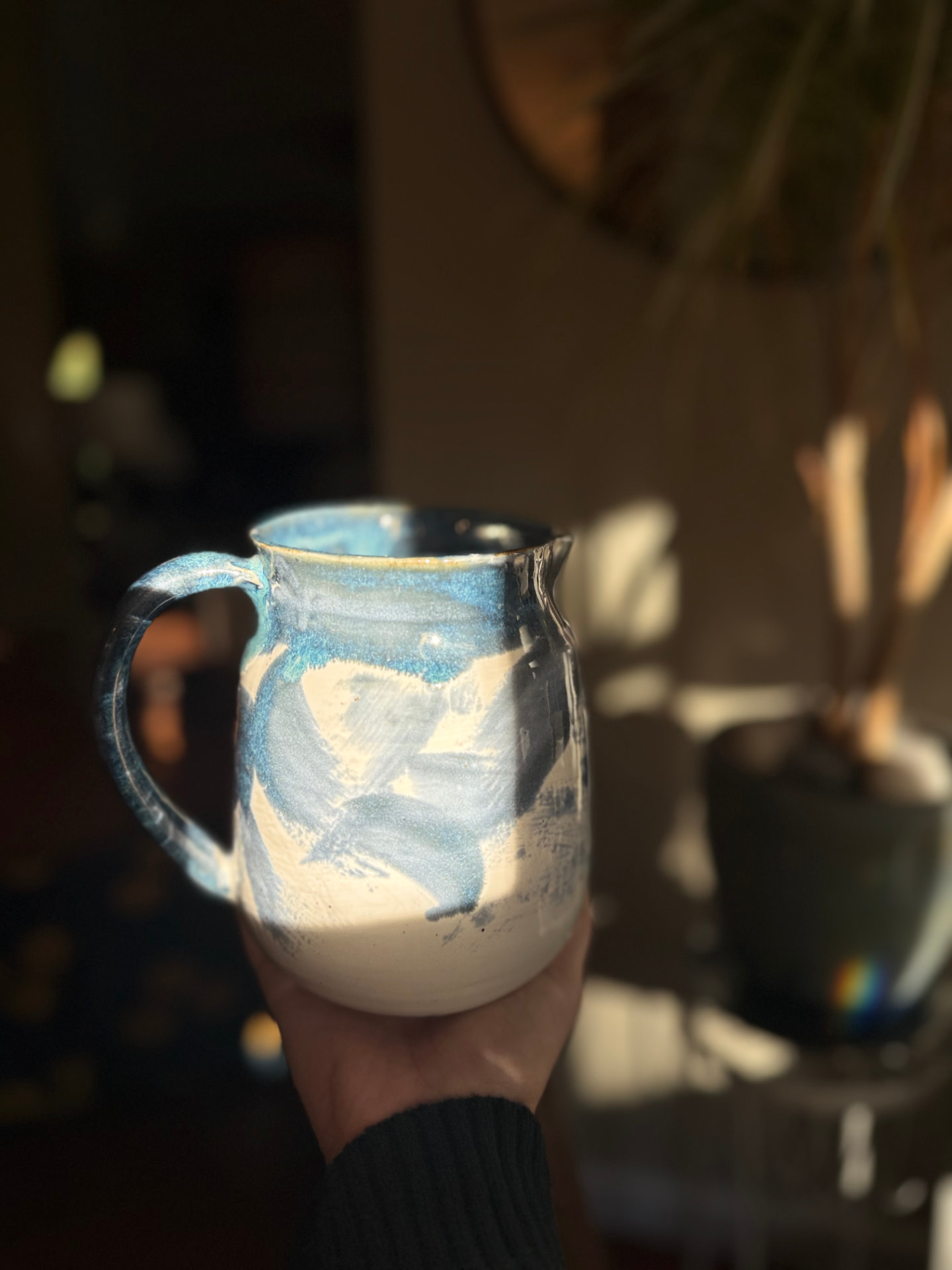 Handmade ceramic pitcher with a mottled teal and slate blue rim and handle, and brushed blue arcs over a cream body