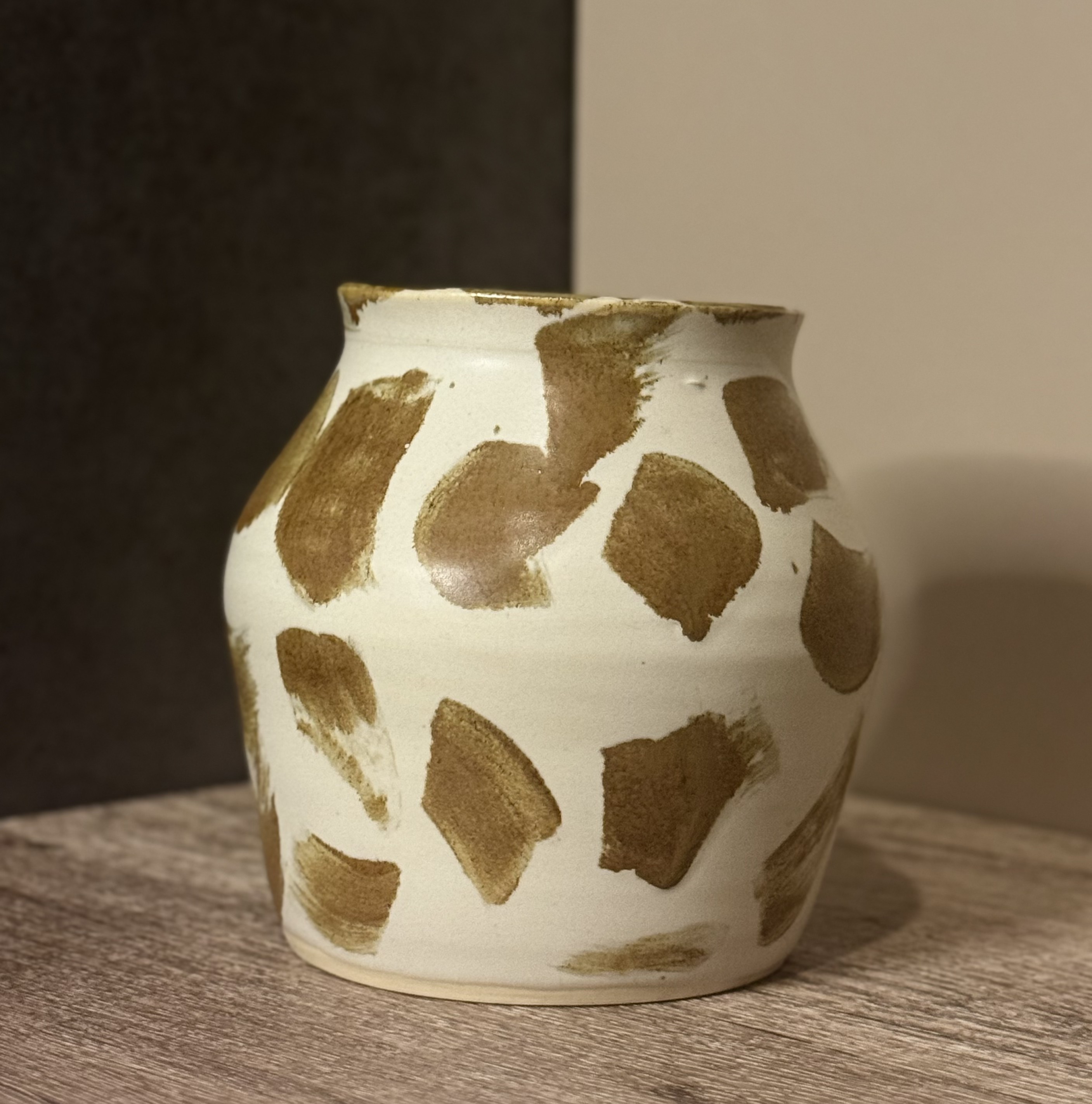 Rounded handmade ceramic vessel with amber brushstrokes over a soft white glaze on a wooden surface