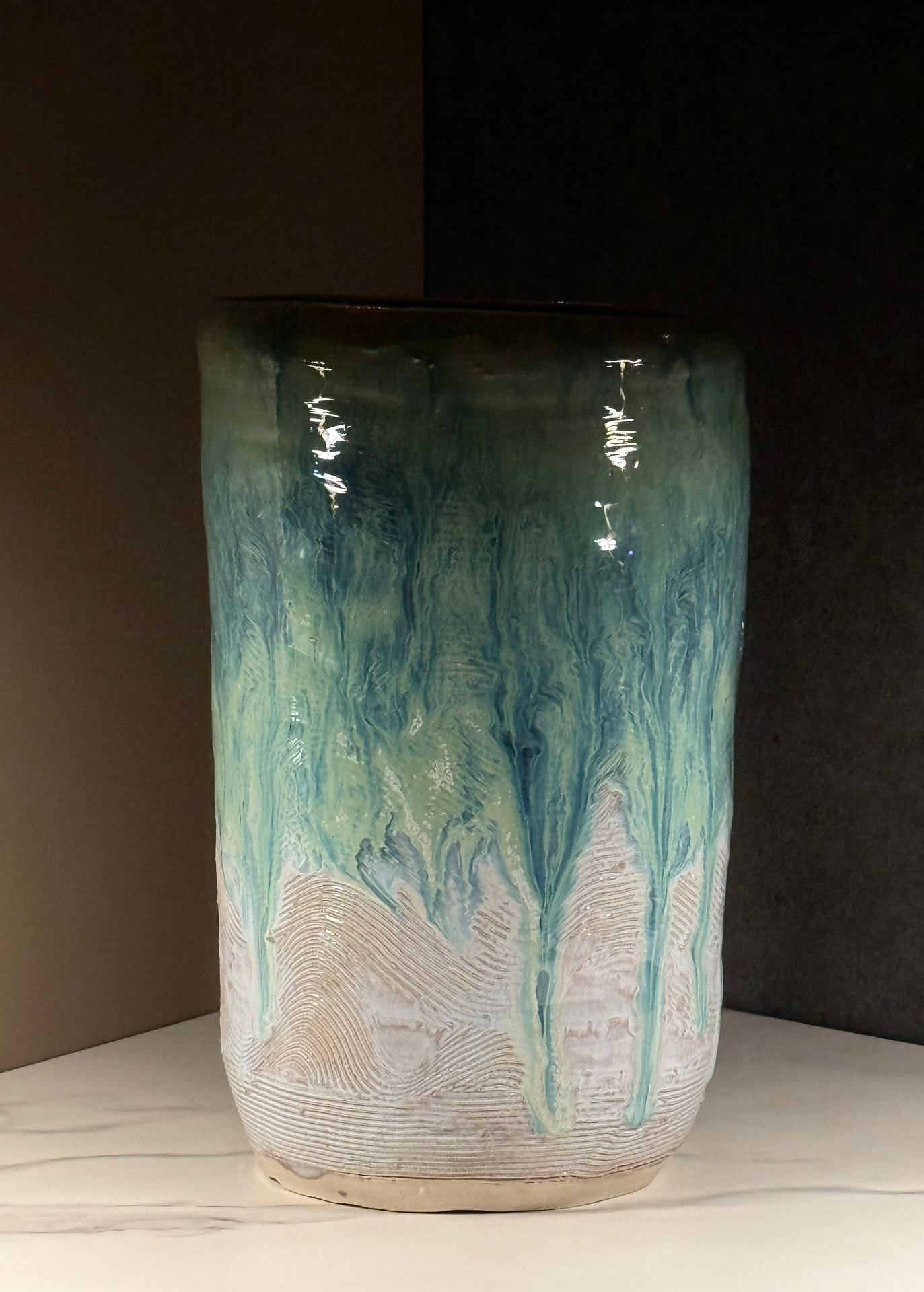 Tall handmade vase with teal and seafoam glaze dripping over carved, combed white clay